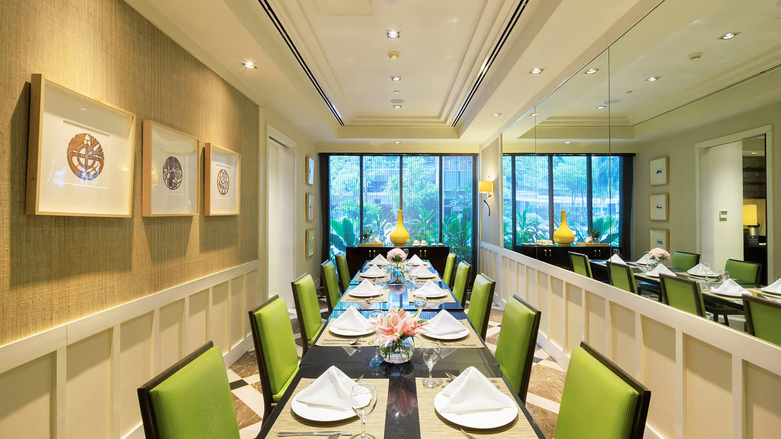 A long banquet table, elegantly set for a gathering, awaits guests in a sun-drenched dining room.